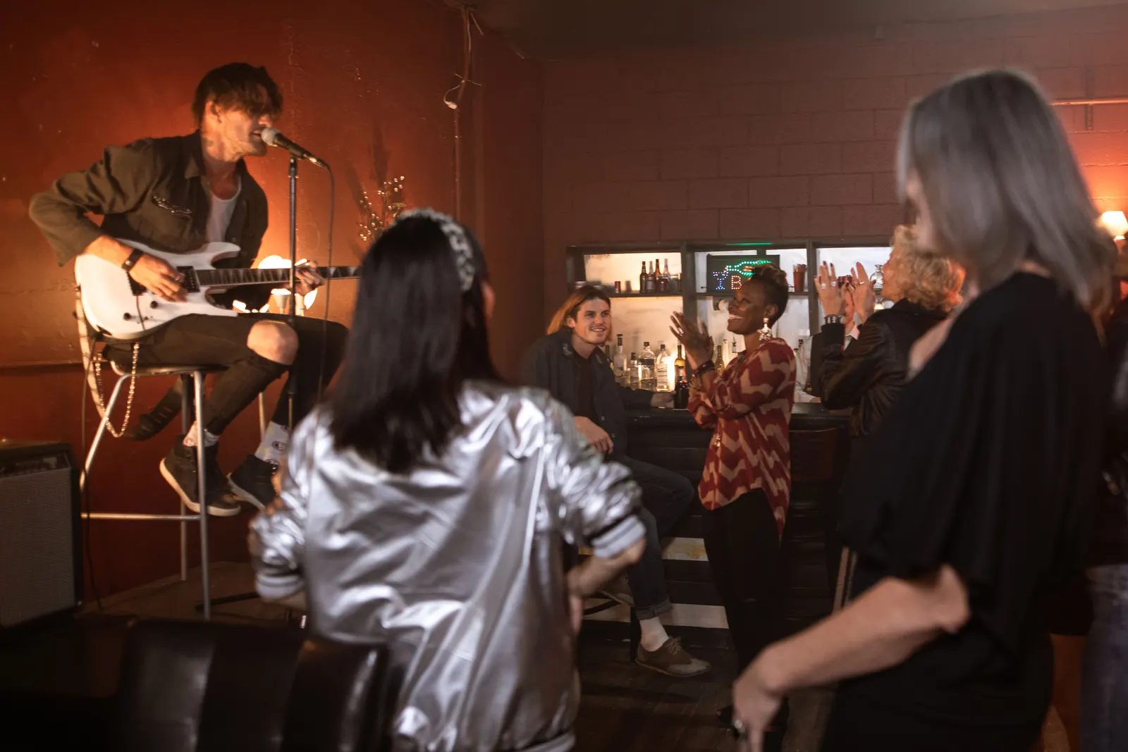 A guitarist playing a live set in a small bar while the audience stands close.