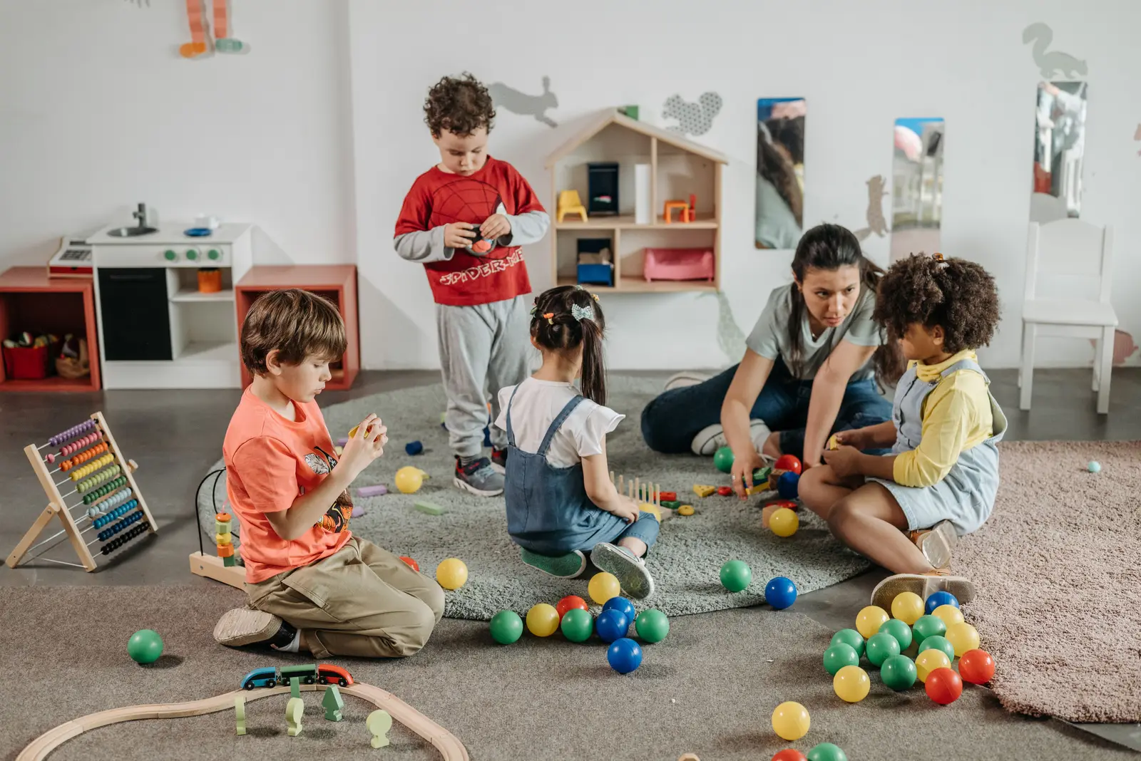 Young children playing with toys on the floor of a nursery room with their teacher.