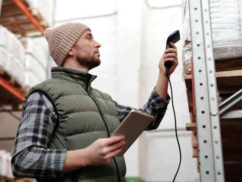A warehouse worker scanning stock on a high shelf with a handheld scanner and tablet
