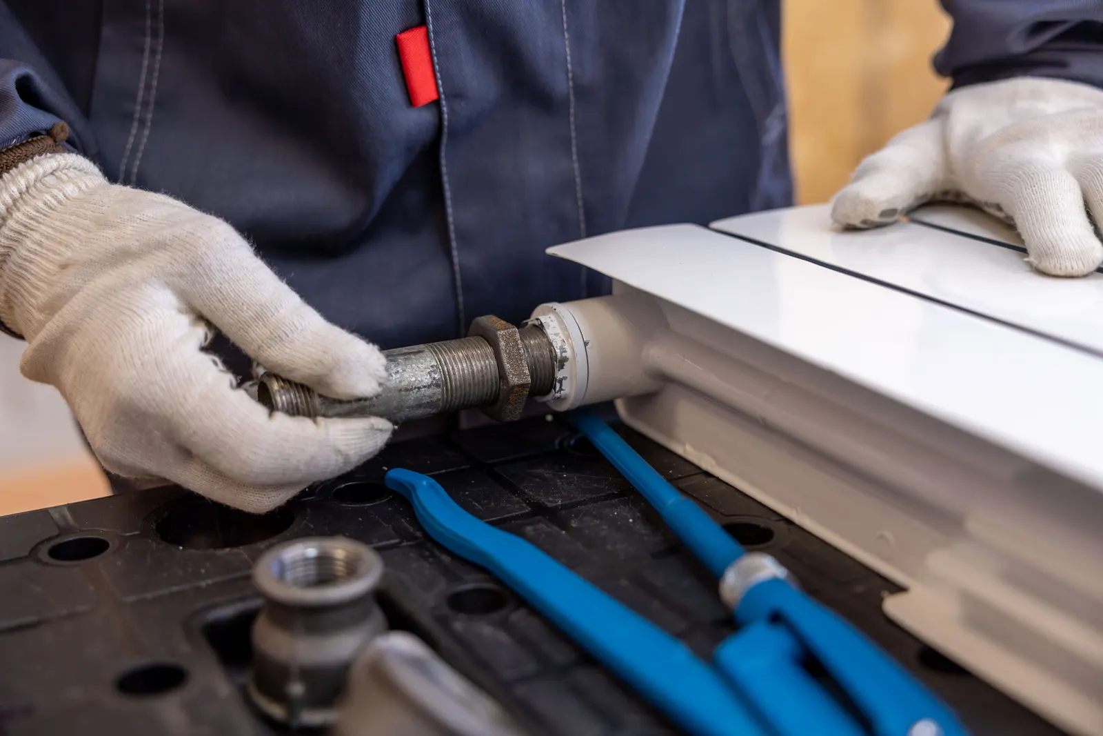 Gloved hands tightening a pipe connection on a radiator with a spanner.