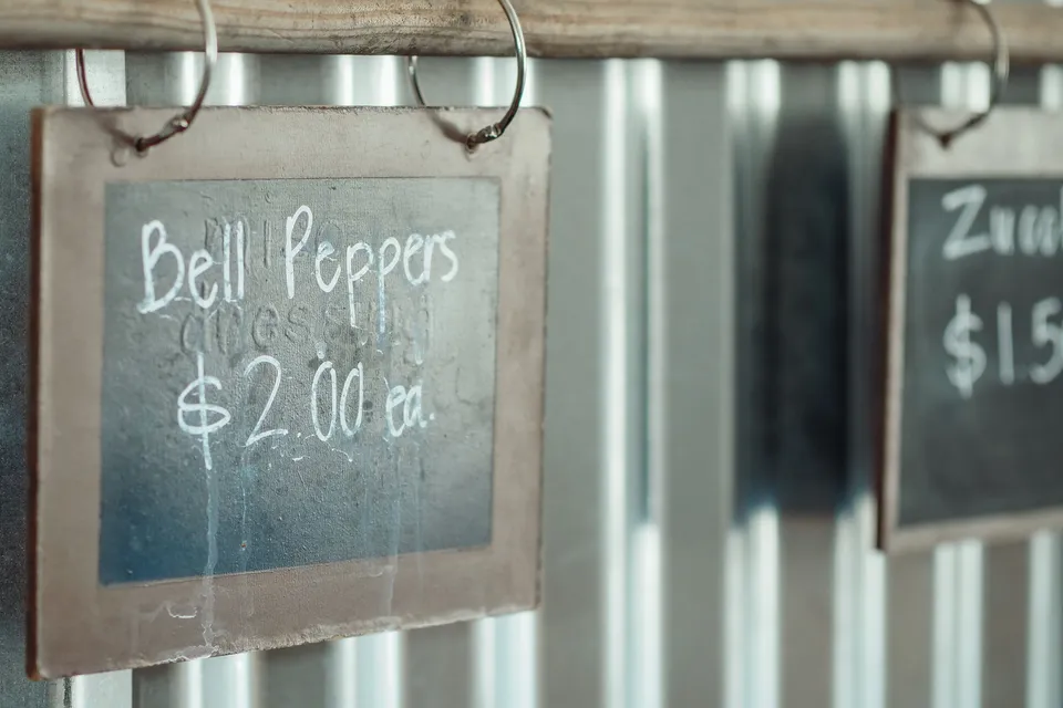 A chalkboard price sign for bell peppers hanging at a market stall.