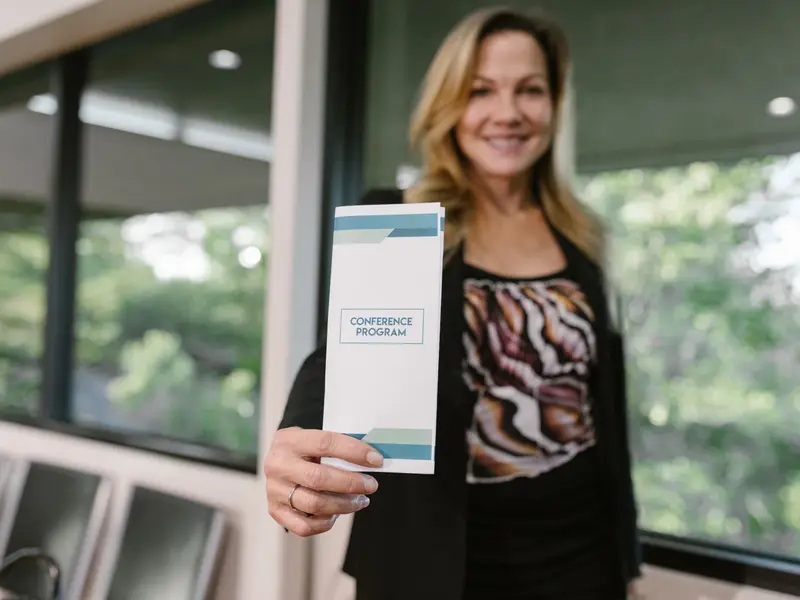 A woman holding up a printed folded conference programme toward the camera