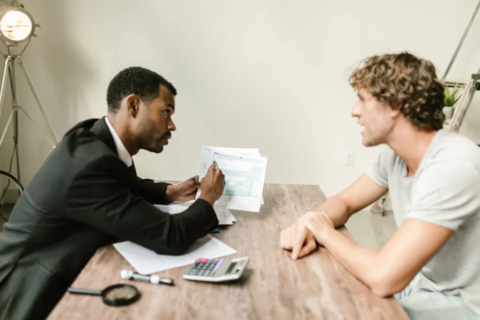 An adviser going through a printed form with a customer across a wooden desk.