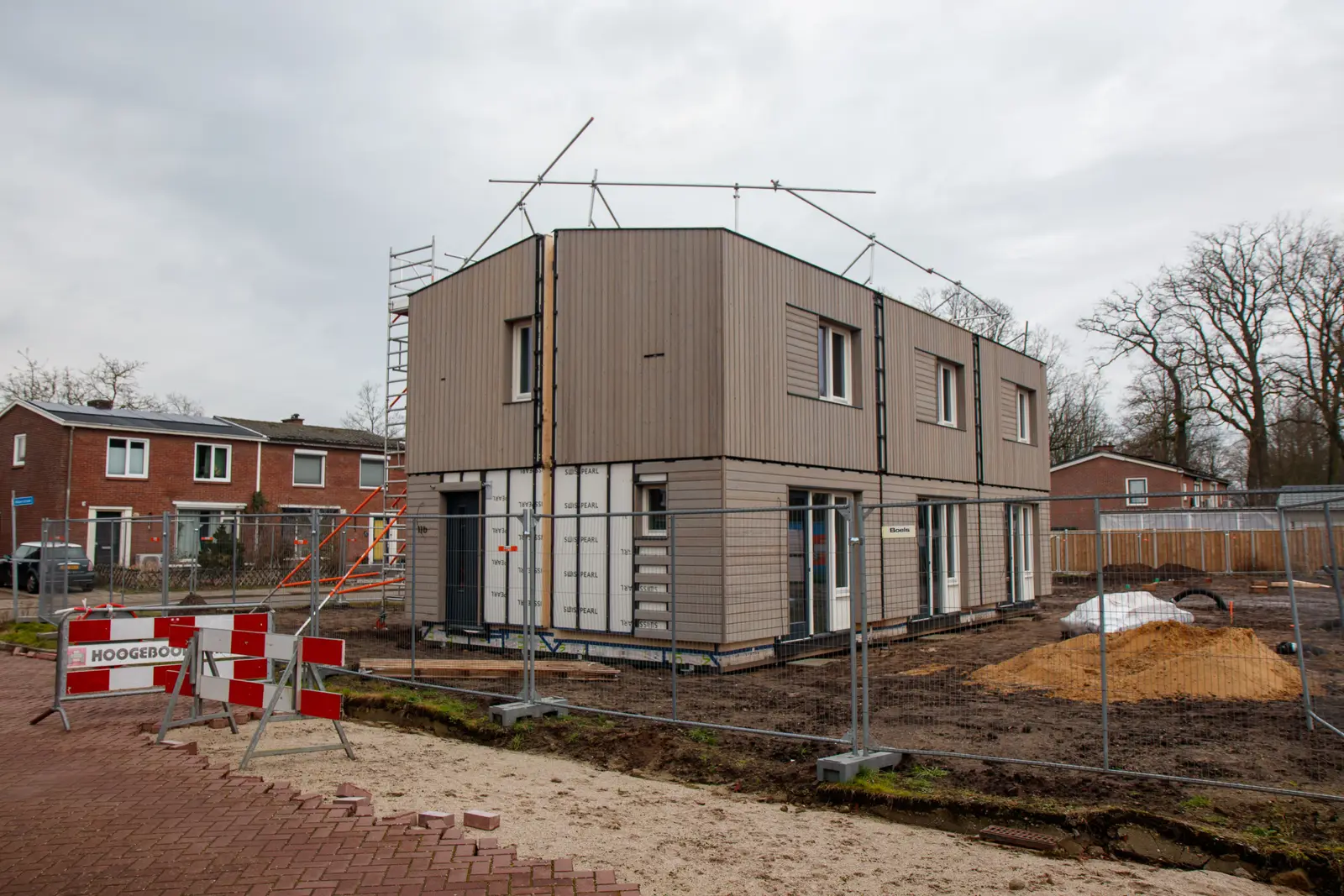 A new house under construction behind site fencing and signs on a cloudy day.