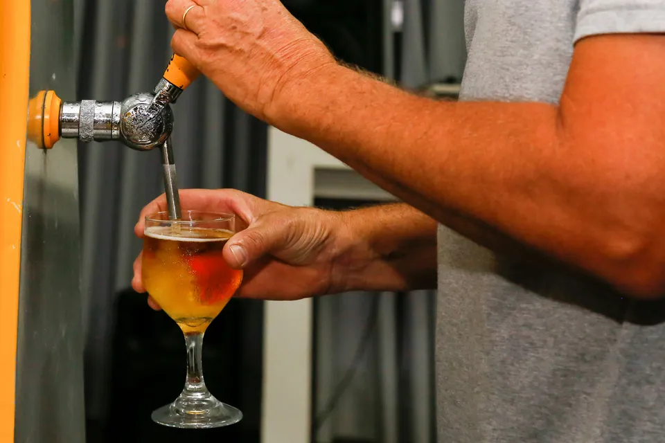 A bartender's hands pouring a draught beer from the tap into a glass.