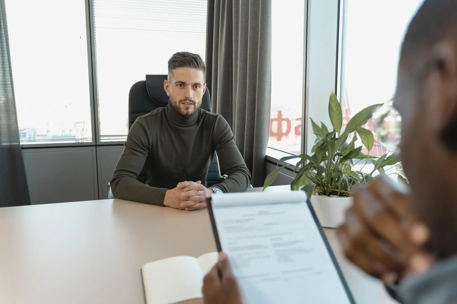 An interview across an office desk, the interviewer holding a printed CV.