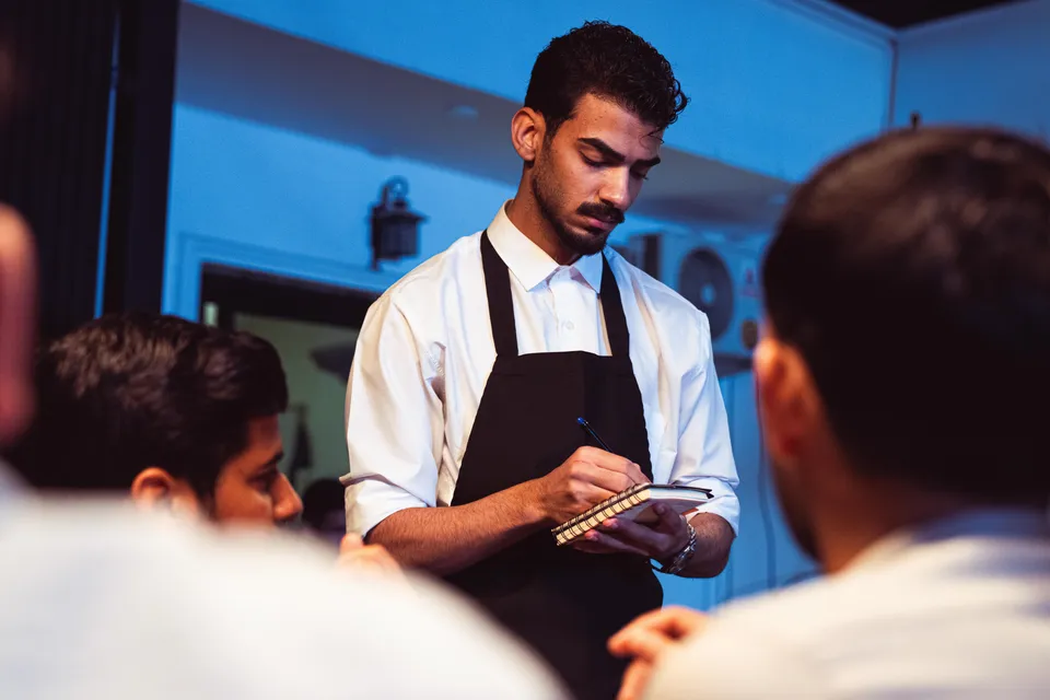 A waiter taking an order on a notepad from a table of guests.