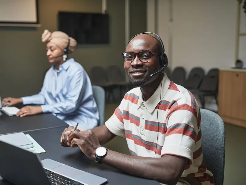 Two customer service staff wearing headsets at their desks, one smiling at the camera
