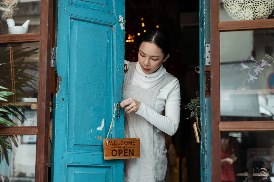 A shop owner hanging an open sign on the blue door of her shop.