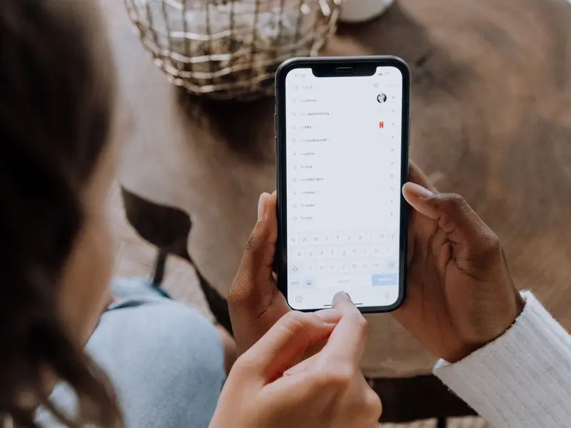 Two hands holding a phone with a search box open and a list of suggested searches