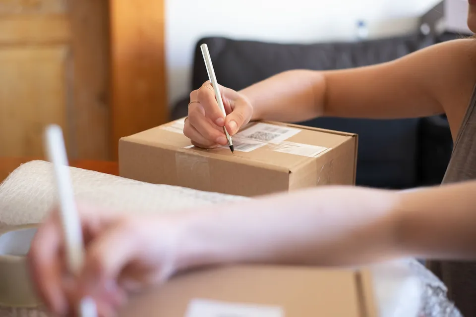 Hands writing a delivery label on a cardboard box ready to send out.