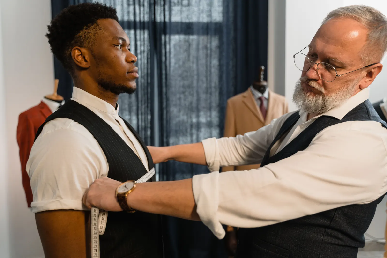 A tailor measuring a customer's arm during a suit fitting.