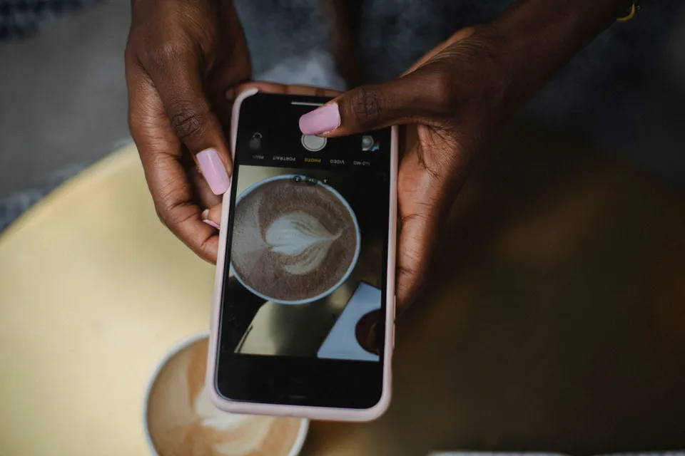 Hands taking a photo of a latte with a phone, seen from above the table.