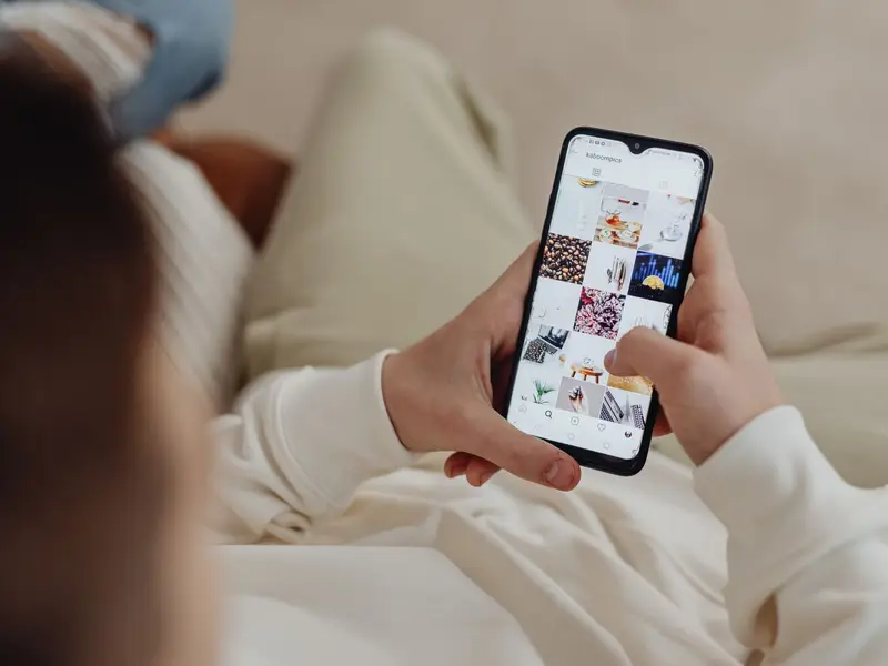 A person relaxing on a sofa scrolling a grid of social media photos on a phone