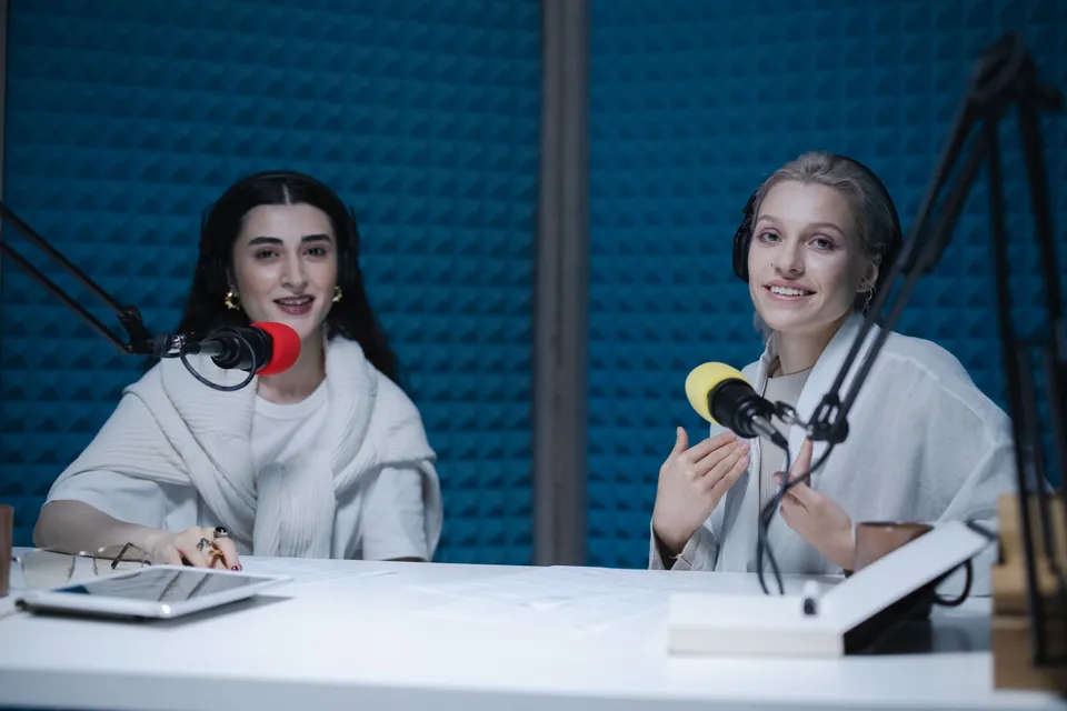 Two women recording a podcast in a soundproofed studio, microphones in front of them.