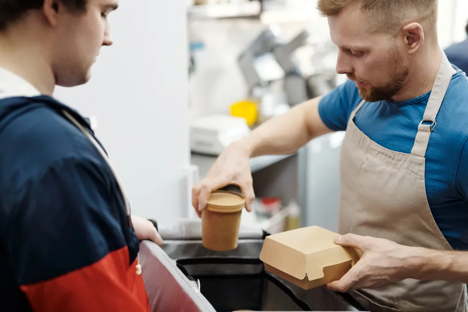 A server packing a takeaway box and cup for a customer waiting at the counter.