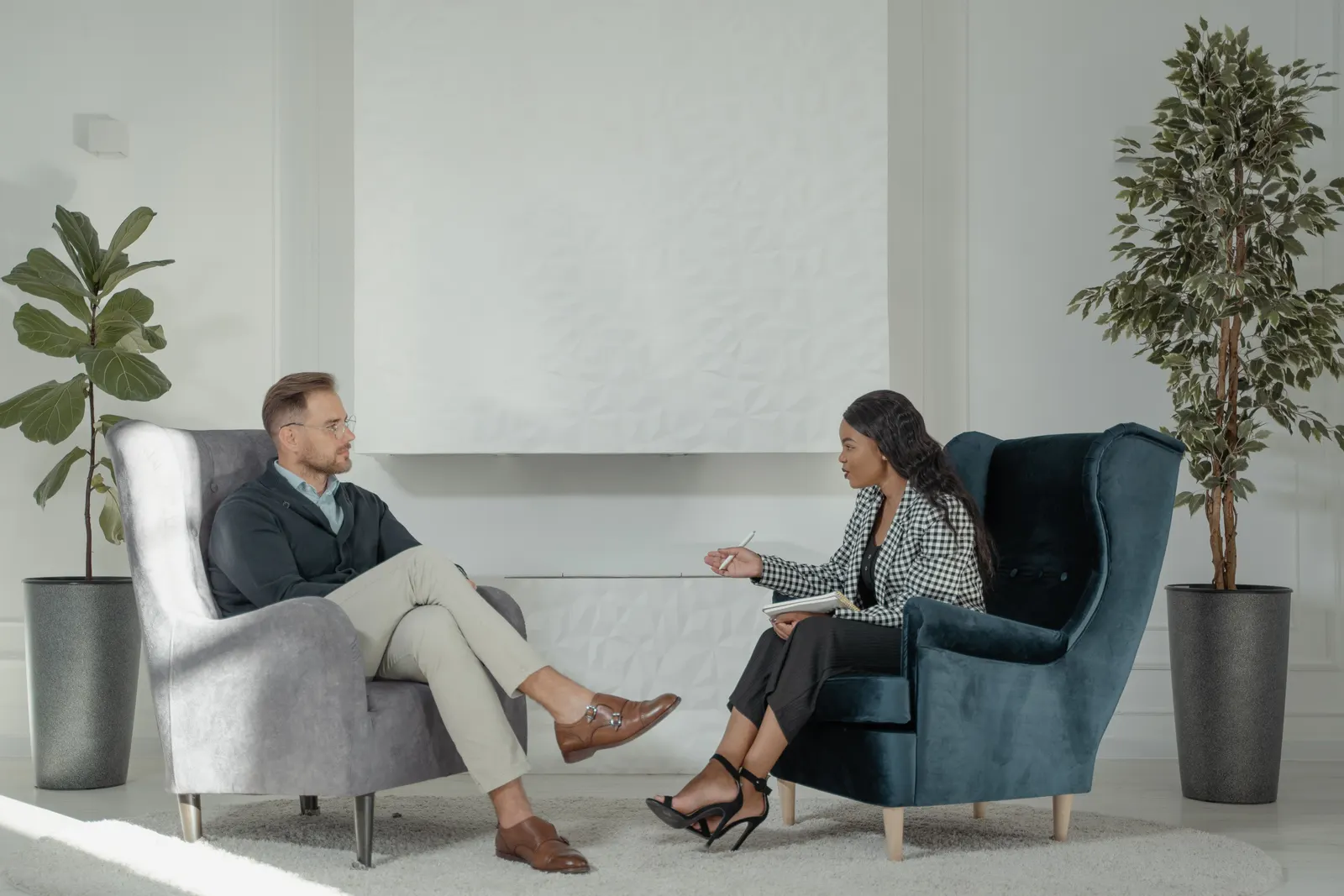 A therapist and the person they are seeing, talking from two armchairs in a quiet, light room.