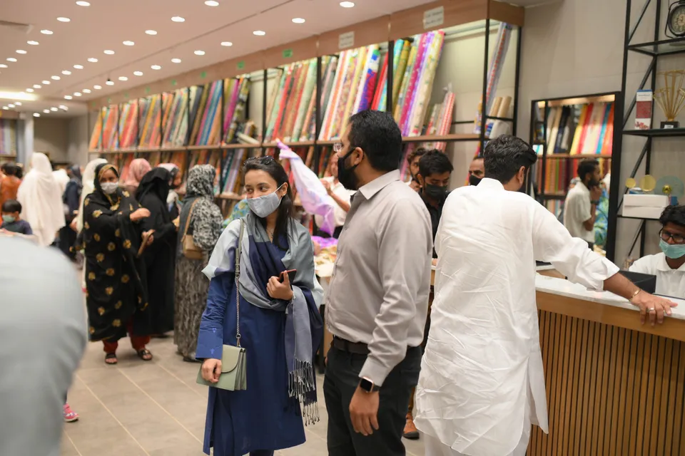 Shoppers browsing a busy fabric shop lined with rolls of cloth.