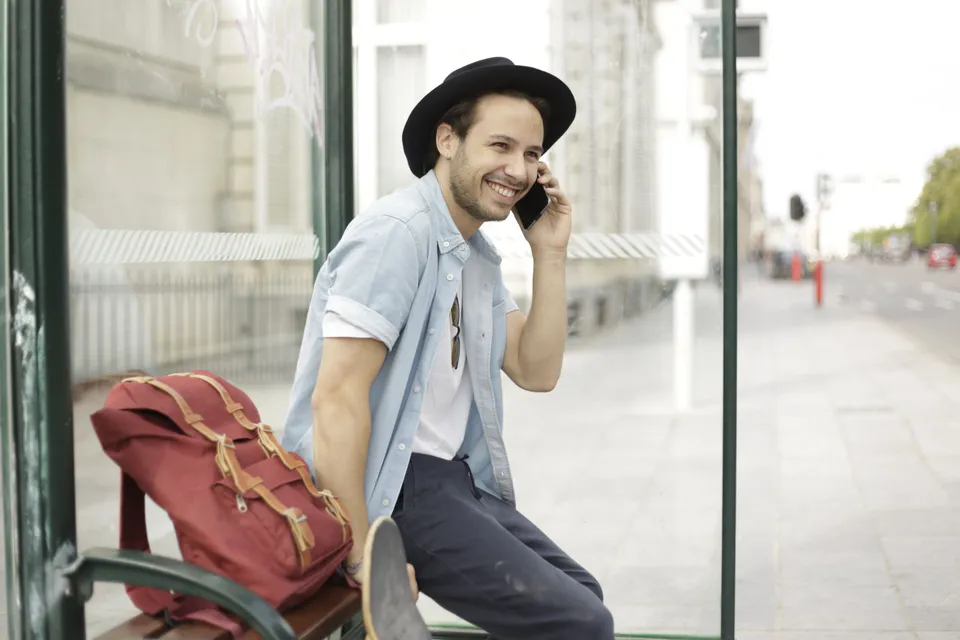 A young man on his phone while waiting at a bus stop.