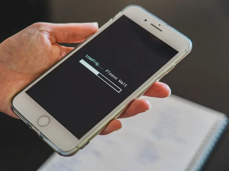 A hand holding a phone whose screen shows a loading bar and the words please wait