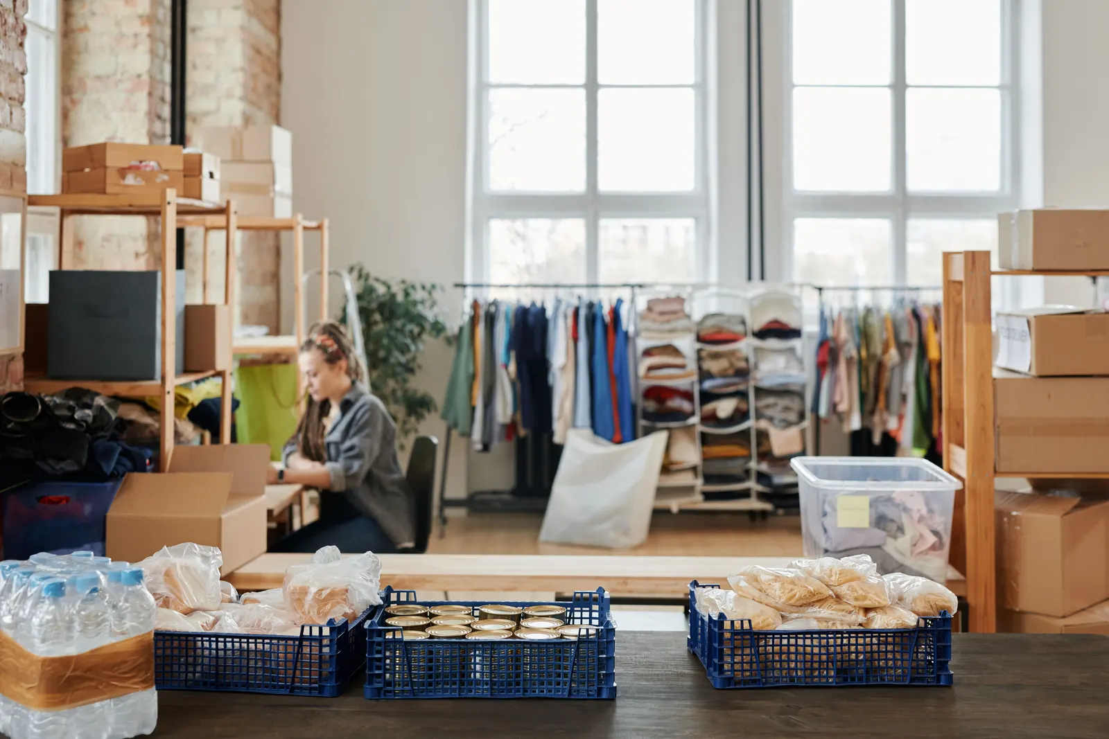A small business stockroom with shelves of boxes, rails of clothing and crates of packed goods.