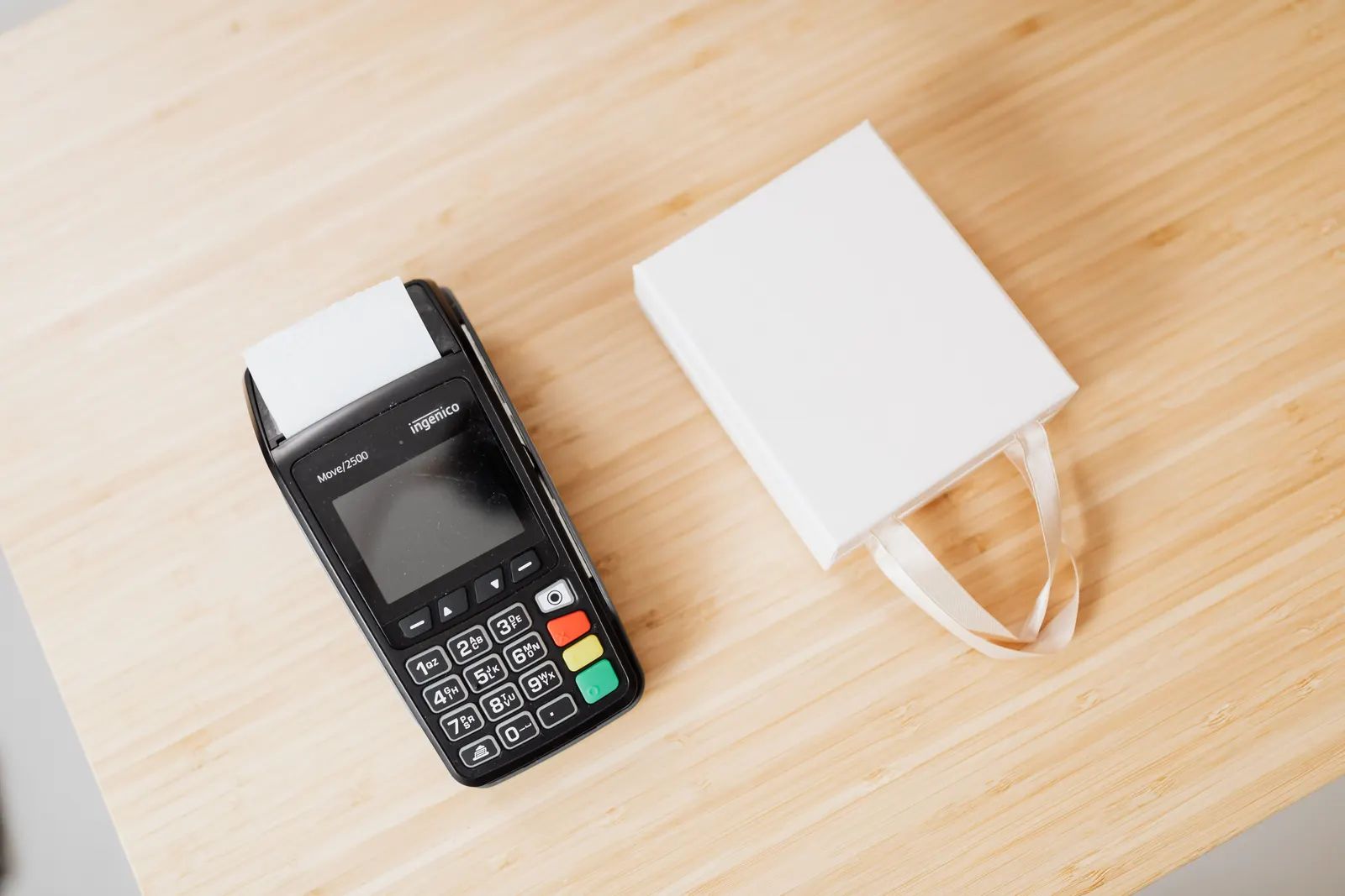 A card payment terminal next to a small white paper bag on a wooden counter.
